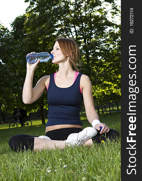 Young girl sitting on the grass drinking water