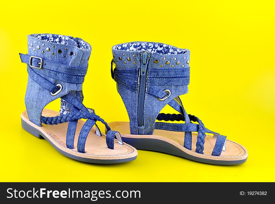 Children sandals sewn from denim stand against a yellow background. Children sandals sewn from denim stand against a yellow background