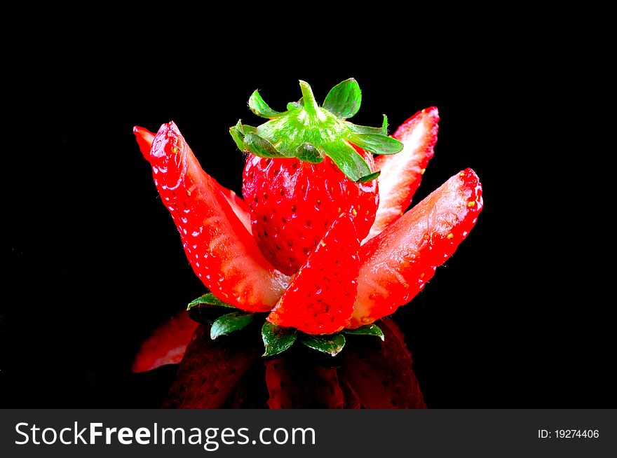 Cut strawberries with green leaves lying against a black background. Cut strawberries with green leaves lying against a black background