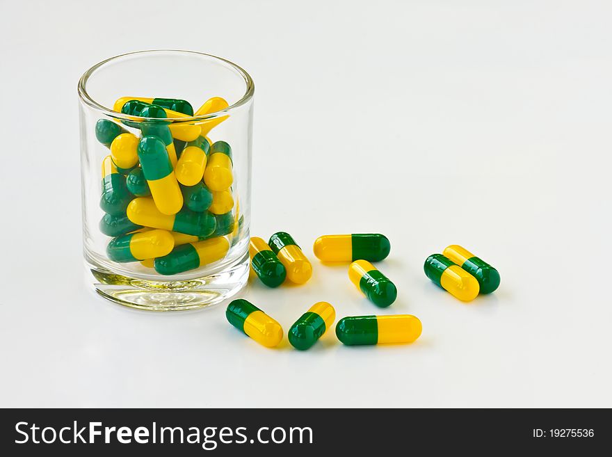 Green and yellow capsule pills in a glass isolated on white background