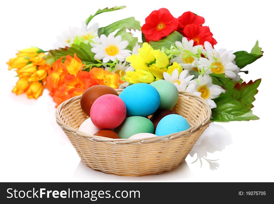 Easter eggs in a wicker basket and flowers isolated on white background