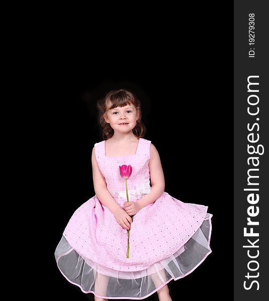 Sweet little girl sitting down with single pink tulip in her hand isolated on black. Sweet little girl sitting down with single pink tulip in her hand isolated on black
