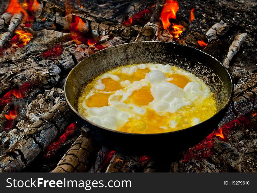 Hiking pan standing on the coals with a roasting in her scrambled eggs. Hiking pan standing on the coals with a roasting in her scrambled eggs.