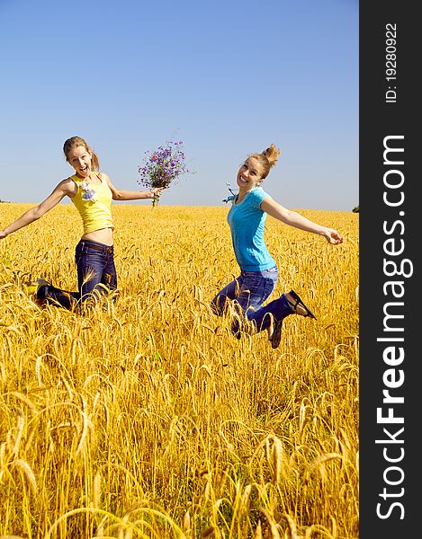 Two beautiful girls jumps in golden field