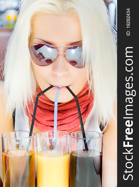 Concept craving and satisfaction Blond woman in sunglasses drinking juice through the sets of three tubes portrait close-up