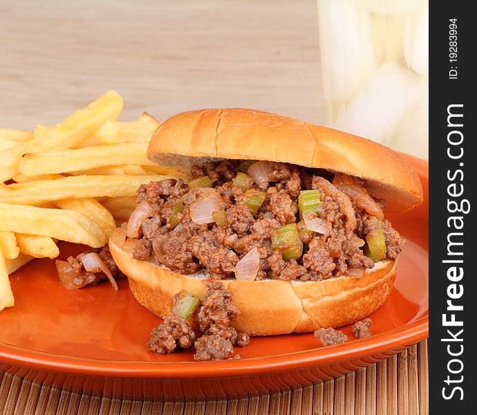 Barbecue beef sandwich on a bun with french fries and a drink in background. Barbecue beef sandwich on a bun with french fries and a drink in background