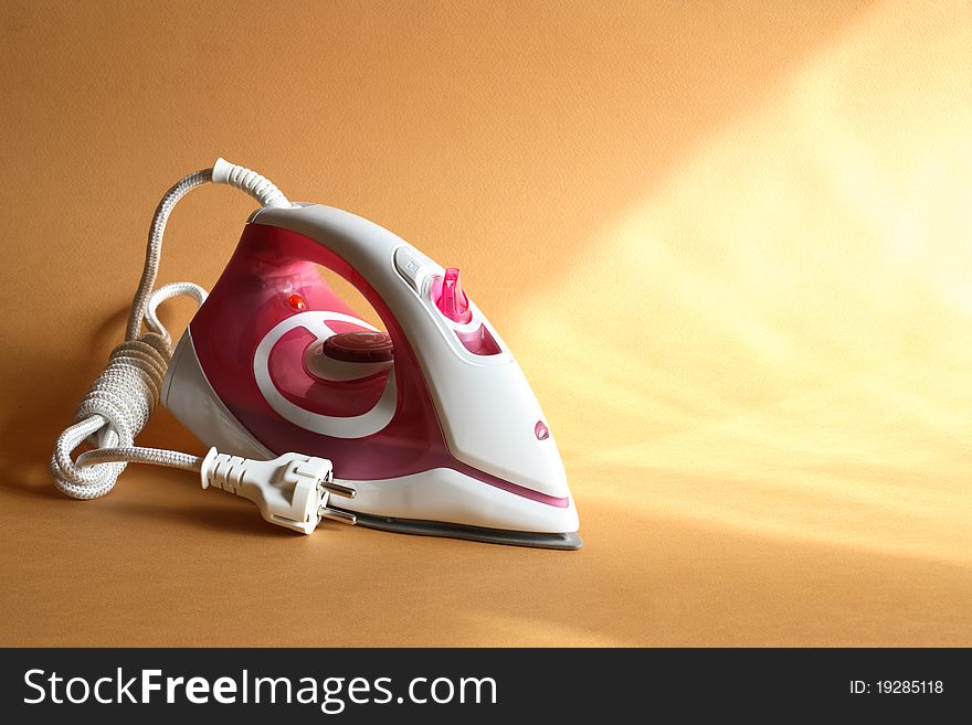 Modern electric iron standing on nice gold background with sun beam