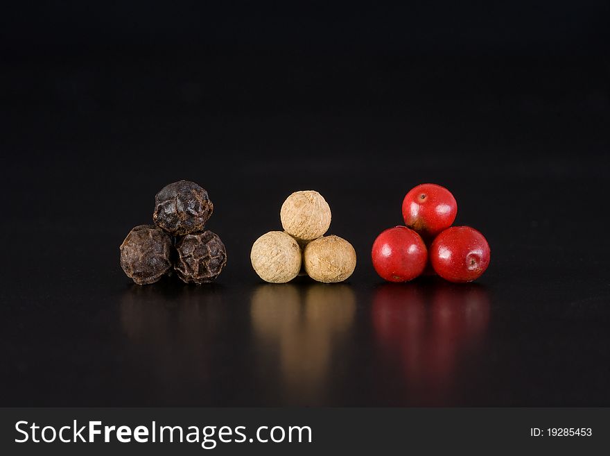Trio of black, white and pink peppercorns isolated on black, macro shot