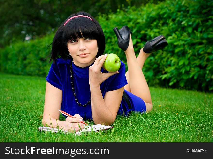 Happy young woman writing in book in countryside with ripe apple, green nature background. Happy young woman writing in book in countryside with ripe apple, green nature background.
