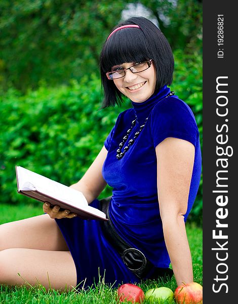 Happy young woman writing in book in countryside with ripe apple, green nature background. Happy young woman writing in book in countryside with ripe apple, green nature background.