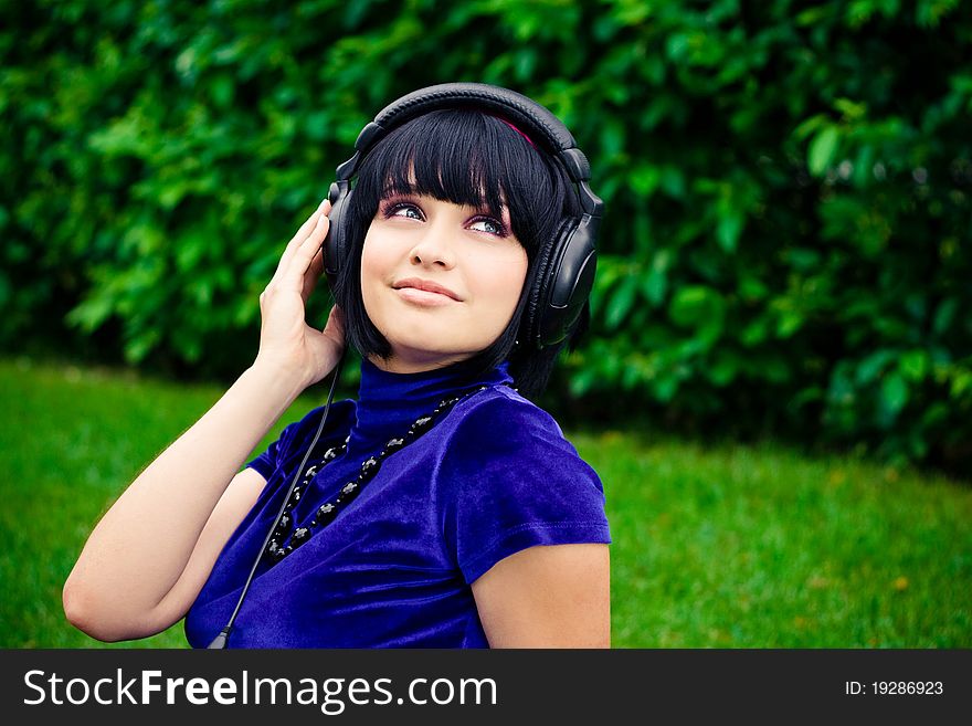 Happy young woman listening to music with headphones; green background. Happy young woman listening to music with headphones; green background.