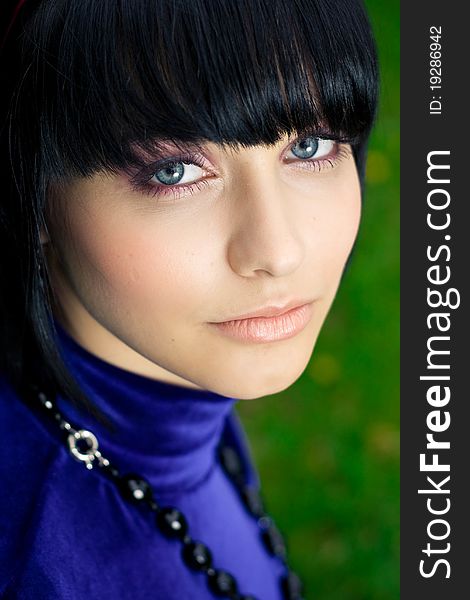 Portrait of attractive young woman with black hair; green nature background