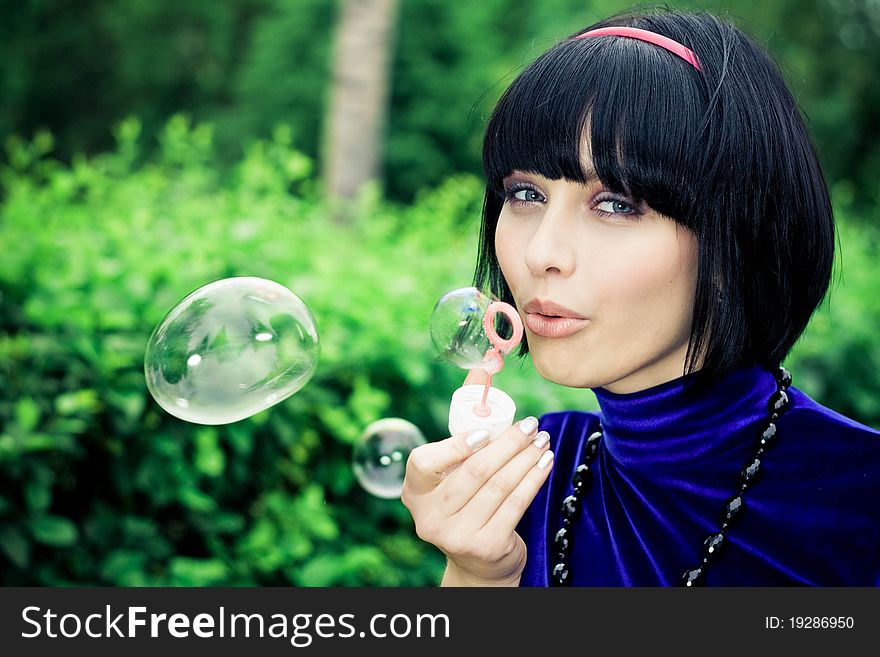 Side view of attractive woman outdoors blowing bubbles; green nature background. Side view of attractive woman outdoors blowing bubbles; green nature background.