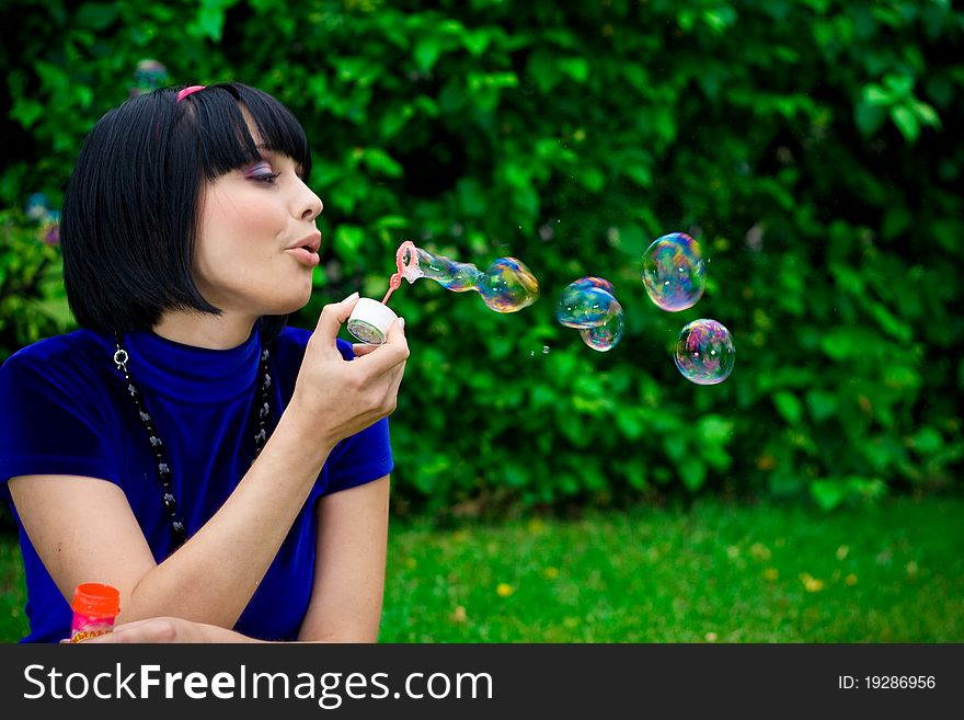 Side view of attractive woman outdoors blowing bubbles; green nature background. Side view of attractive woman outdoors blowing bubbles; green nature background.