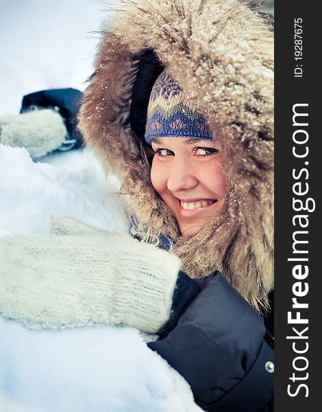 Attractive young woman in wintry coat with large fur head, snowy in background.