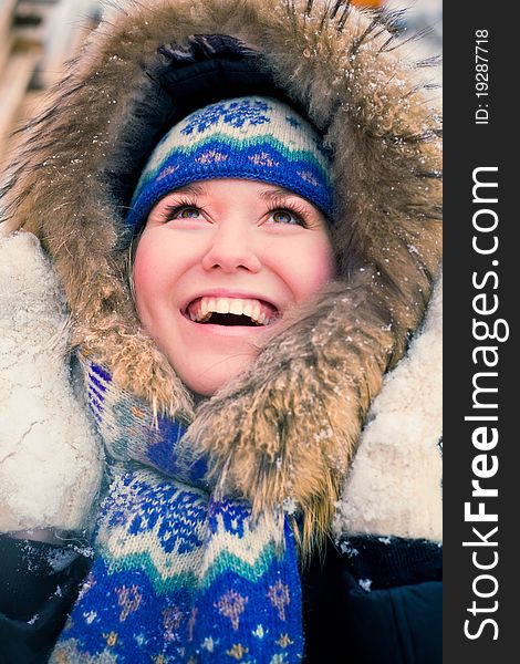 Attractive young woman in wintry coat with large fur head, snowy in background.