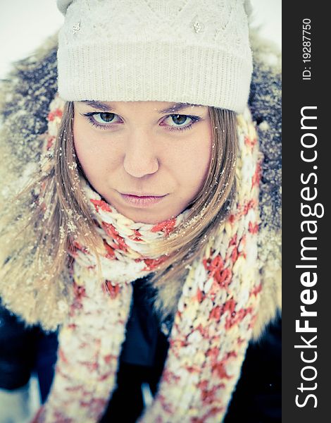 Attractive young woman in wintry coat with large fur head, snowy in background.