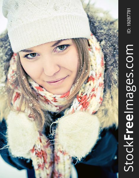 Attractive young woman in wintry coat with large fur head, snowy in background.