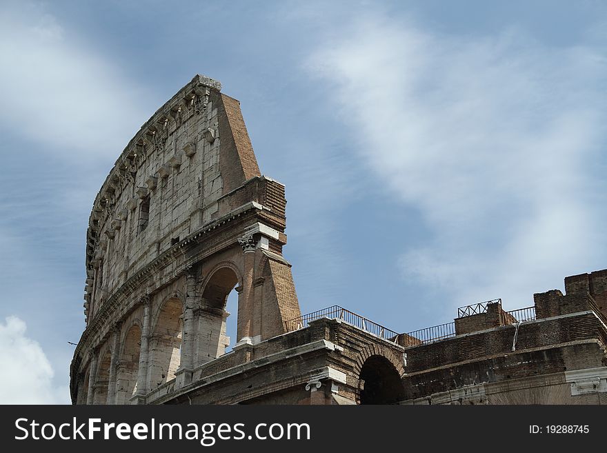 Daytime image of the Roman Coliseum with bright sun and partly cloudy skys.