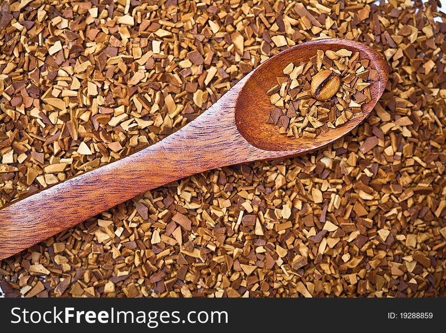 Closeup of a coffee bean in a wooden spoon surrounded soluble coffee. Closeup of a coffee bean in a wooden spoon surrounded soluble coffee