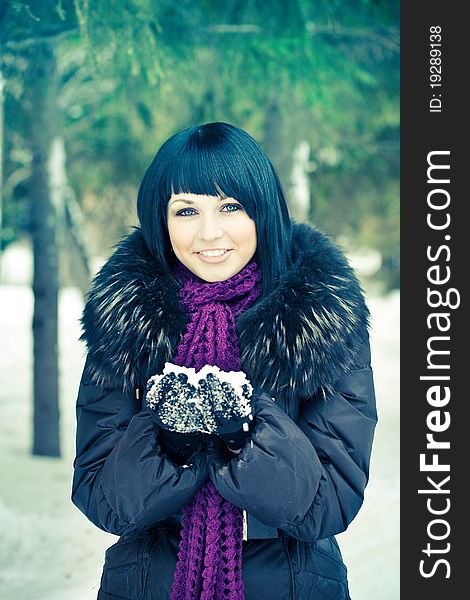 Attractive young woman in wintry coat with large fur head, snowy in background.