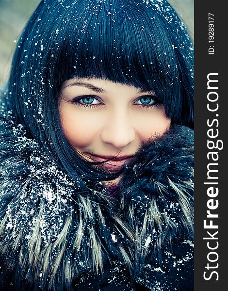 Attractive young woman in wintry coat with large fur head, snowy in background.