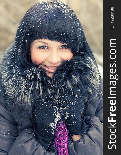 Attractive young woman in wintry coat with large fur head, snowy in background.