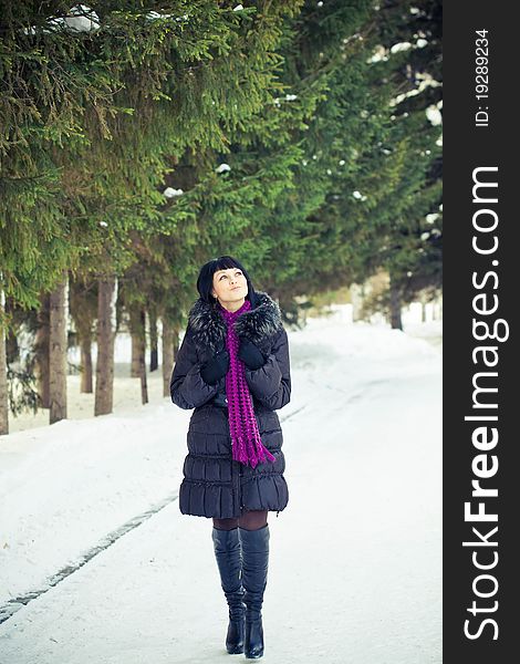 Attractive young woman in wintry coat with large fur head, snowy in background.