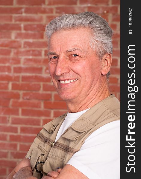 Old builder in the uniform on a brick background. Old builder in the uniform on a brick background
