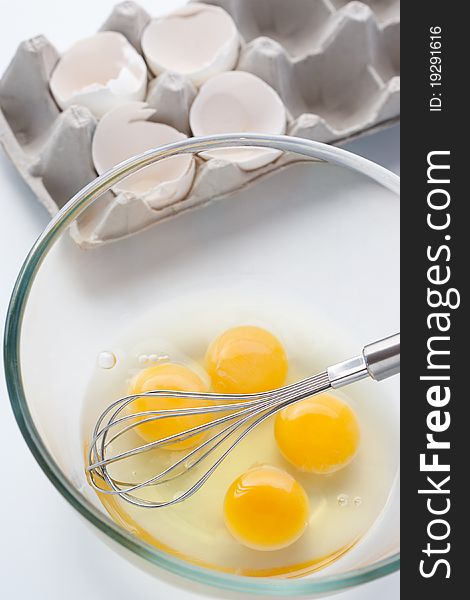 Cooking, whisk with eggs in a bowl and egg shells, over white background.