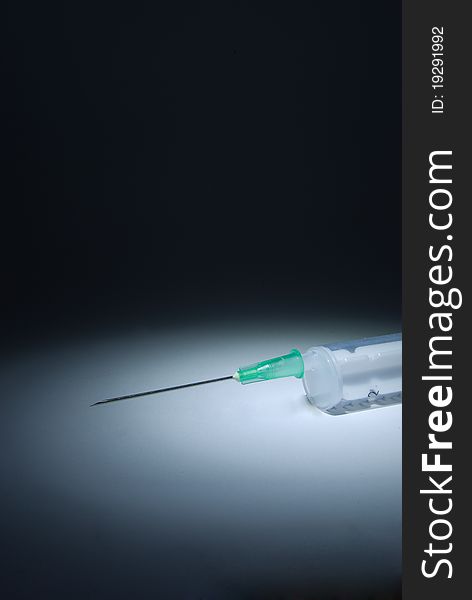 A plastic syringe with hypodermic needle on dark background