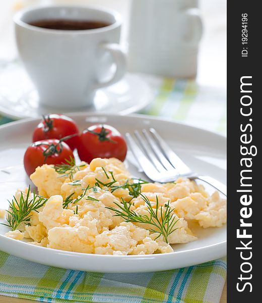 A plate of creamy scrambled eggs garnished with dill, a cup of coffe with milk. A plate of creamy scrambled eggs garnished with dill, a cup of coffe with milk