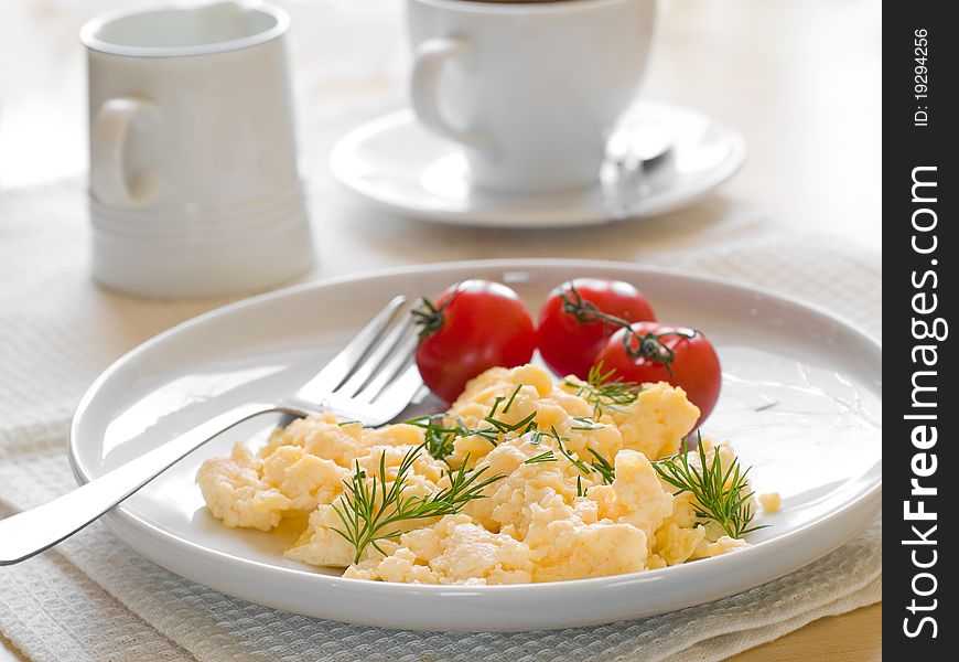 A plate of creamy scrambled eggs garnished with dill, a cup of coffe with milk. A plate of creamy scrambled eggs garnished with dill, a cup of coffe with milk