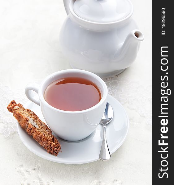 Cup of tea with cookie near the teapot  on white table