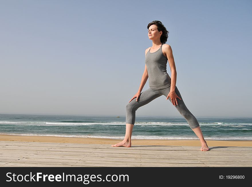 Image of the young woman in grey wear doing exercises on the beach. Image of the young woman in grey wear doing exercises on the beach