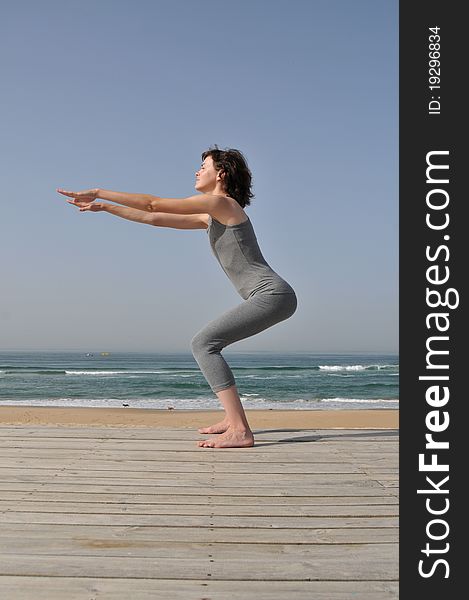 Image of the young woman in grey wear doing exercises for legs on the beach. Image of the young woman in grey wear doing exercises for legs on the beach