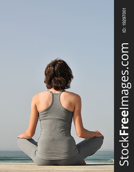 Image of the young woman in grey wear sitting and doing meditation yoga exersices  on the beach. Image of the young woman in grey wear sitting and doing meditation yoga exersices  on the beach