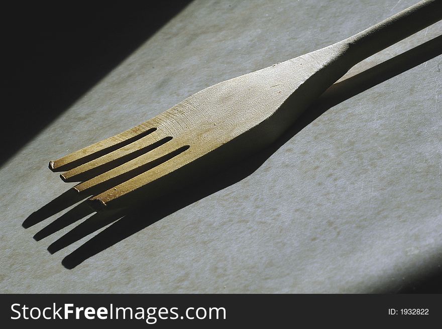A wooden fork utensil used for cooking sitting on a counter in the sunlight.