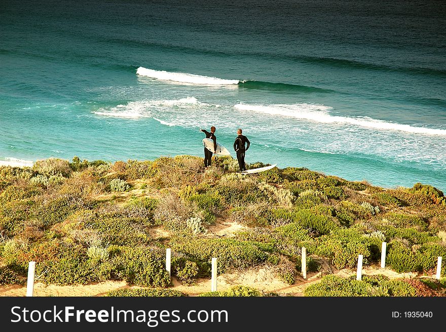 Surfers stand on top of sand hill and contenplate waves. Surfers stand on top of sand hill and contenplate waves