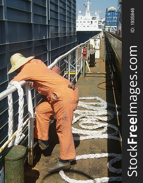 Sailor dressed in orange overall with a hat, watching the loading of a large steel module onboard a freight ship. Sailor dressed in orange overall with a hat, watching the loading of a large steel module onboard a freight ship.
