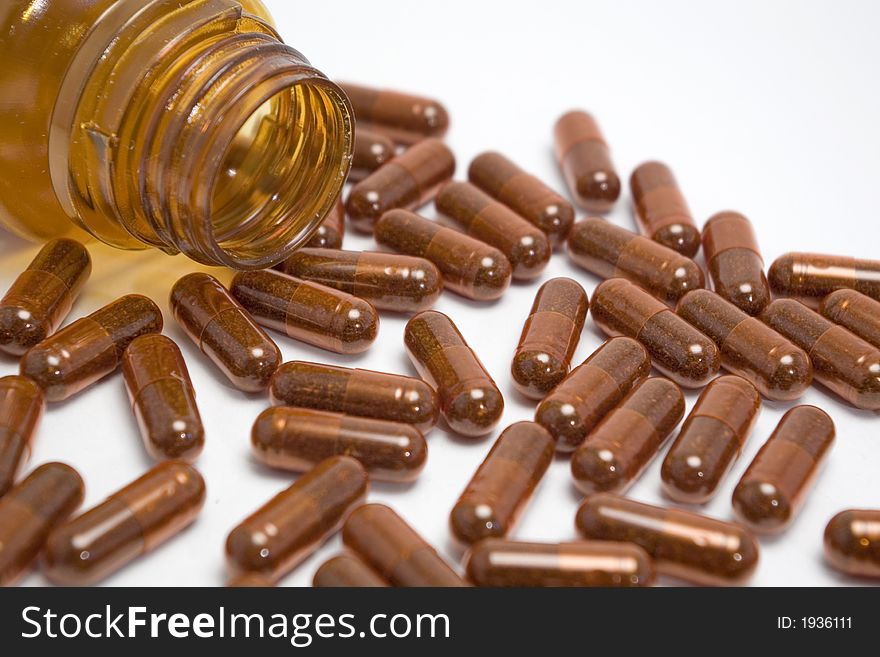 Brown pills spilled next to the bottle over white background