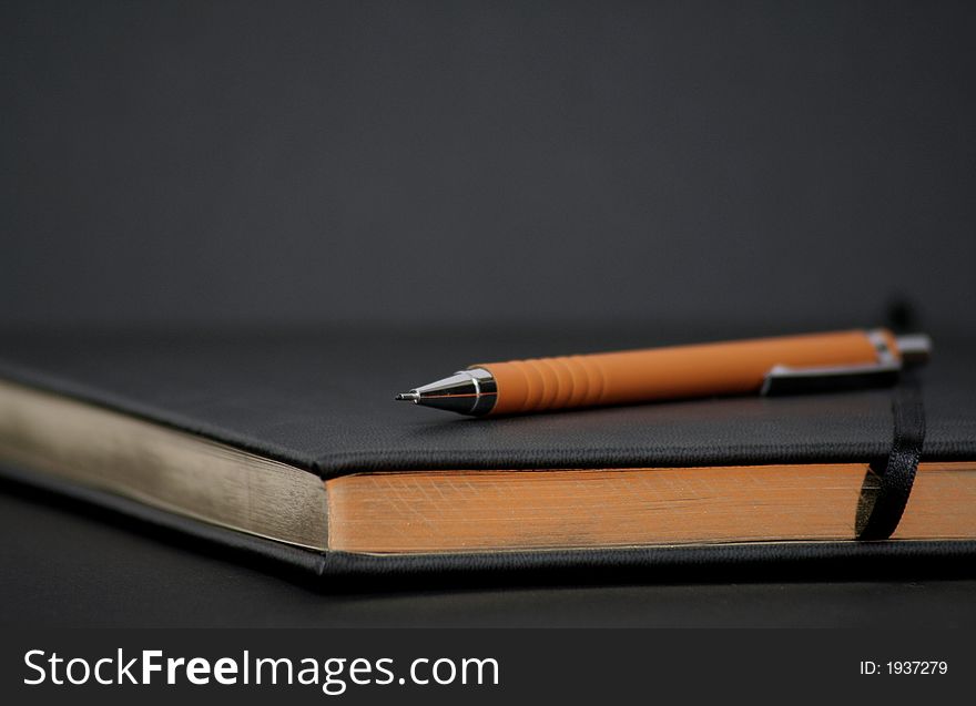 Writing book with golden pages and an orange pencil above. Writing book with golden pages and an orange pencil above