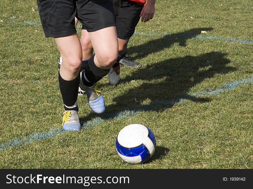 A challenging forward is chasing the soccer ball in an attempt to make a goal.