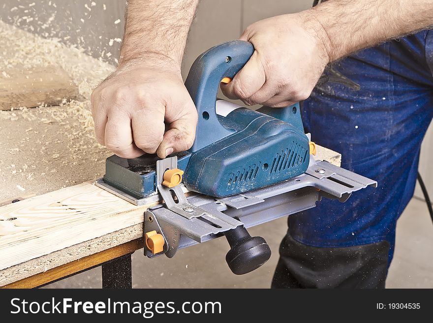 Close-up of a construction worker's hand and power tool while planing a piece of wood trim for a project. Close-up of a construction worker's hand and power tool while planing a piece of wood trim for a project.