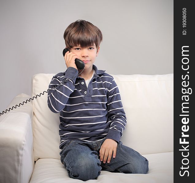 Child sitting on a sofa and talking on the telephone