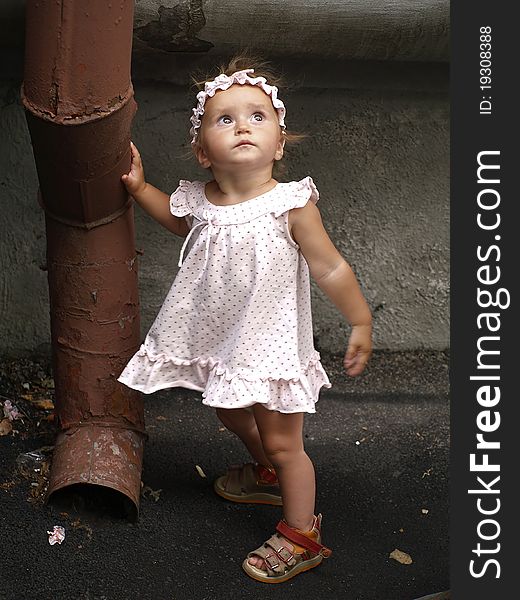 Small girl wearing a dress, leaning against a rainwater pipe against grey wall. Small girl wearing a dress, leaning against a rainwater pipe against grey wall