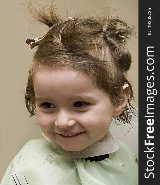 Small girl at hairdresser's, wearing hairpins and a cape, smiling