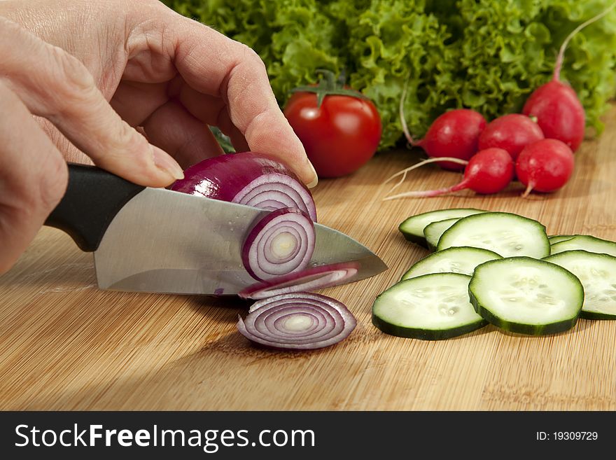 An onion is cutting on a cutting board. Ready Cucumber slices are lying on board. An onion is cutting on a cutting board. Ready Cucumber slices are lying on board.