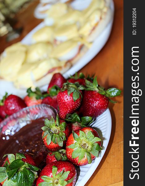 Some ripe strawberries sit around a bowl of chocolate dip with oter desserts in the background. Some ripe strawberries sit around a bowl of chocolate dip with oter desserts in the background.