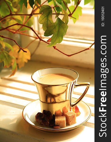 Coffee in gold cup with brown sugar and blured leaves on background